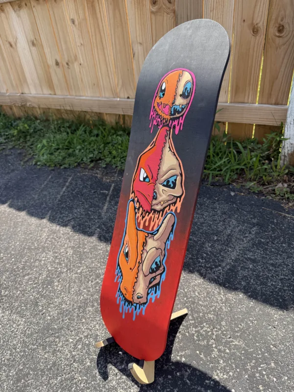 Side view of the hand-painted skateboard deck with drippy skull evolutions of Charmander, Charmeleon, and Charizard. Neon tones and gloss finish emphasize fiery textures.