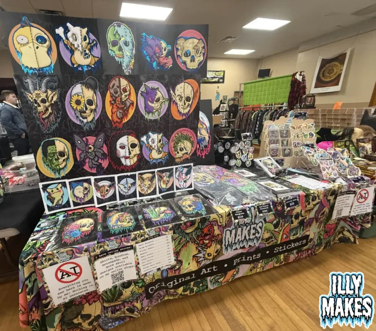 My illymakes art booth setup at the Buffalo Horror Garage Sale, featuring drippy skull paintings, prints, and stickers on display.