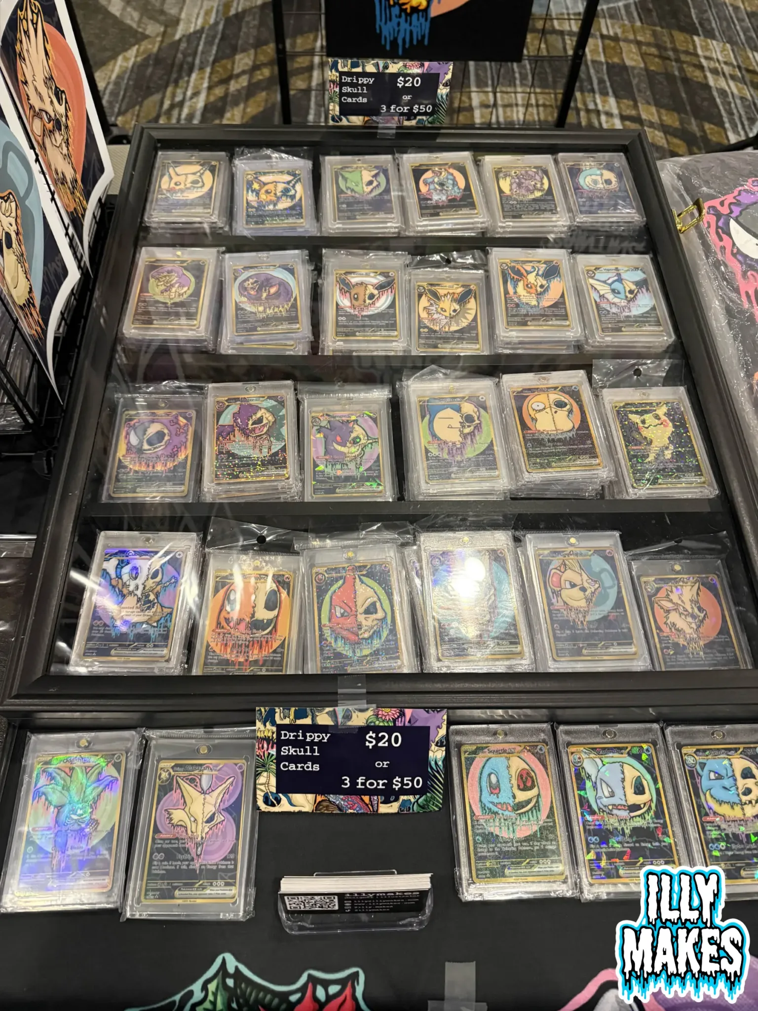 Close-up view of my merch table featuring drippy skull prints, Pokémon skull stickers, and original canvas paintings.