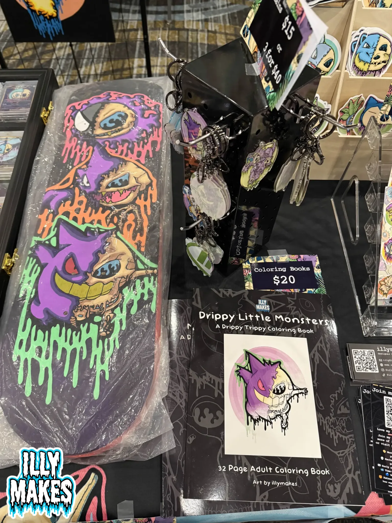 Close-up view of my merch table featuring drippy skull prints, Pokémon skull stickers, and original canvas paintings.