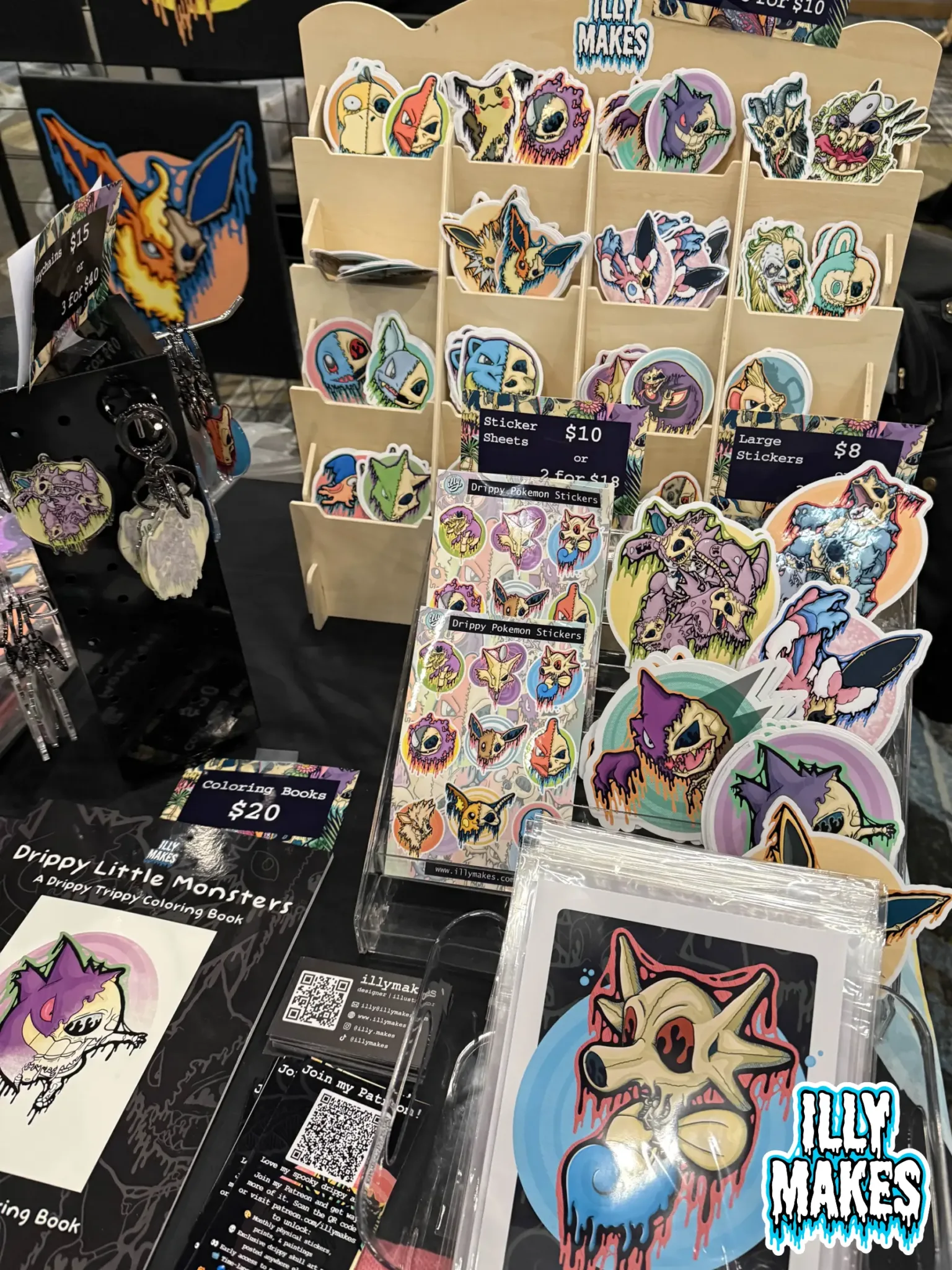 Close-up view of my merch table featuring drippy skull prints, Pokémon skull stickers, and original canvas paintings.